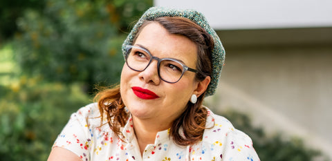Frau mit grauer Vintage-Kunststoffbrille, Blümchenkleid & rotem Lippenstift – stilvoll & zeitlos.