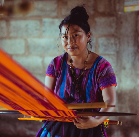 Asiatische Frau in buntem Kleid webt Stoff – kunstvoller Stil & Brillen-Statement.