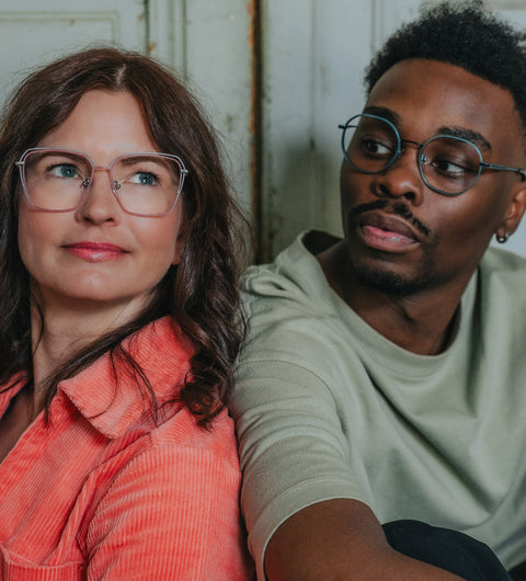 Schicke Frau im orangen Anzug und stilvoller farbiger Mann mit ENNY Brillen – ausdrucksstarkes Design vom Optiker, für alle Facetten.