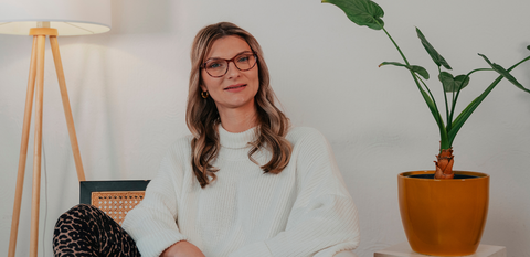 Junge Frau mit Brille sitzt elegant und lässig in einer cleanen Umgebung. Sie trägt das ENNY Modell Glücksbote.