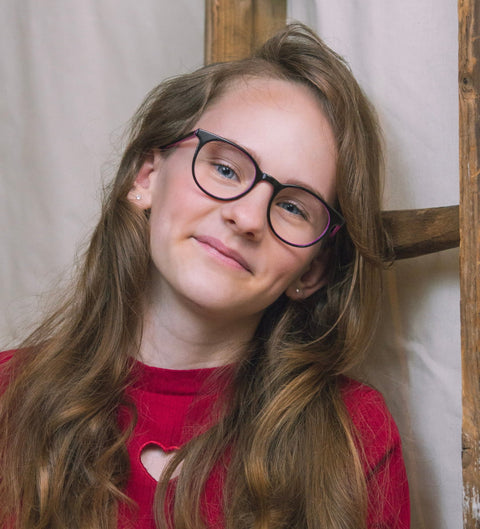 Mädchen trägt runde Kinderbrille in Dunkelbraun mit pinker Innenseite im Alltag