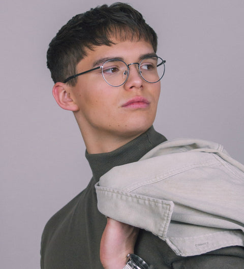 Junger Mann mit Kurzhaarschnitt trägt die ENNY Brille „Sico“ in Gunmetal, runde Form – stylischer, selbstbewusster Blick über die Schulter