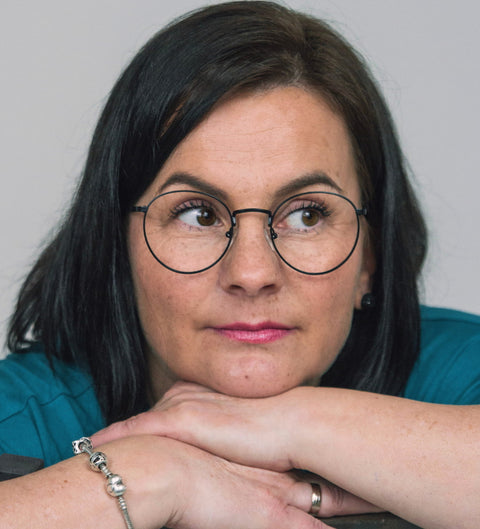 Frau mit schwarzem Bob lehnt nachdenklich auf den Armen und trägt die ENNY Brille „Sico“ in runder Form in mattem Schwarz, schlicht und zeitlos