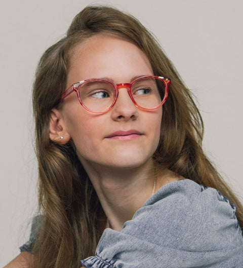 Mädchen mit langen braunen Haaren trägt die runde Kinderbrille Turi in halbtransparentem Erdbeerrot und blickt zur Seite