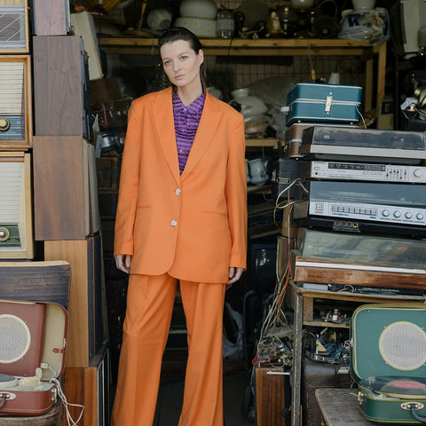 Stilvolle Frau im orangen Anzug in einem Retro-Laden mit alten Radios – Vintage-Vibes pur.
